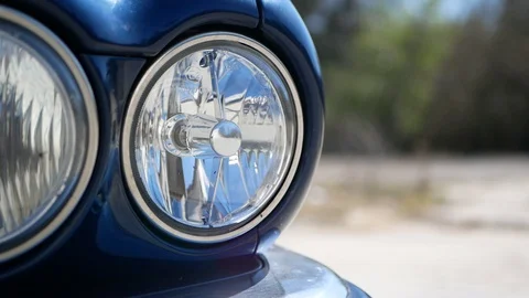 Front headlights of old blue classic Jaguar with pan movement Stock Footage 128101381