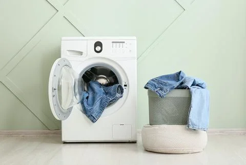 Front load washing machine with denim clothes and laundry basket Stock Photos