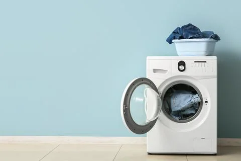 Front load washing machine with denim clothes and laundry basket Stock Photos