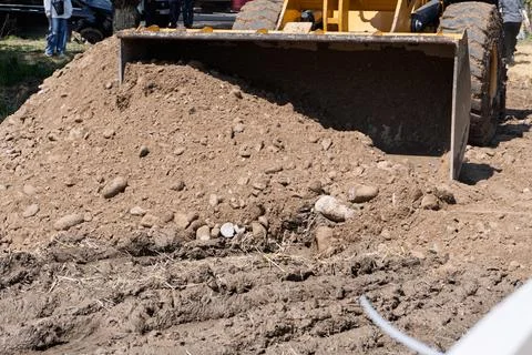 Front loader bucket filled with dirt and stones on a muddy construction site Stock Photos