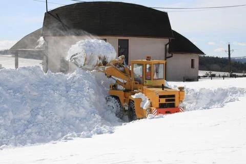 Front loader clears large piles of snow near rural buildings in winter, Stock Photos
