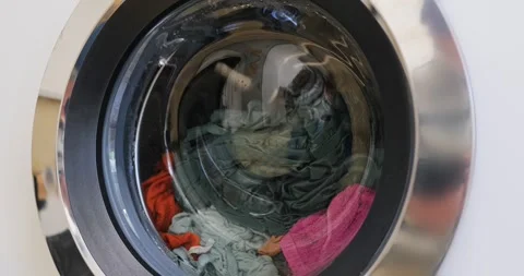 Front loading washing machine drum spinning with colorful laundry in motion Video stock 331775238