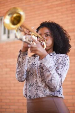 Front low angle view of a young female street musician playing the trumpet with Stock Photos