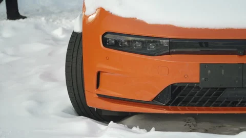 Front of orange electric car covered in snow, with owner feet passing nearby. Stock Footage 329224368