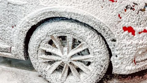 Front right wheel of a red car on which foam is applied to wash a car at a self Stock Photos
