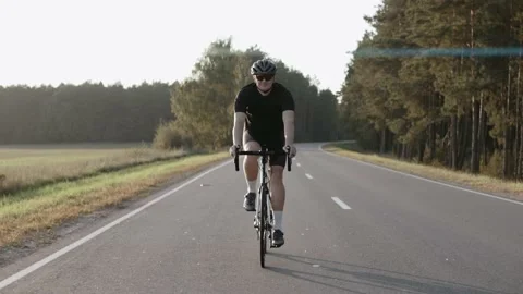 Front shot of man riding a road bike at the sunset on a highway, wearing helmet 스톡 동영상 166174011