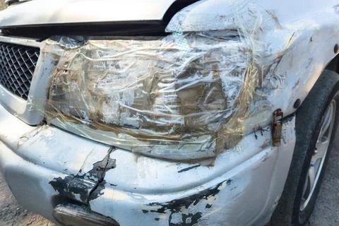 Front side of an old damaged white vehicle headlamp fixed with clear tape Фото