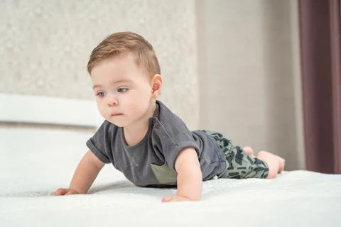 Front side view of blond haired pretty crawling baby on the bed on a white sheet Foto stock