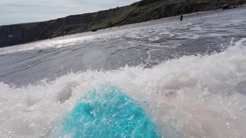 Front of surfboard as it rides a wave in to the beach Stock Footage 272618154