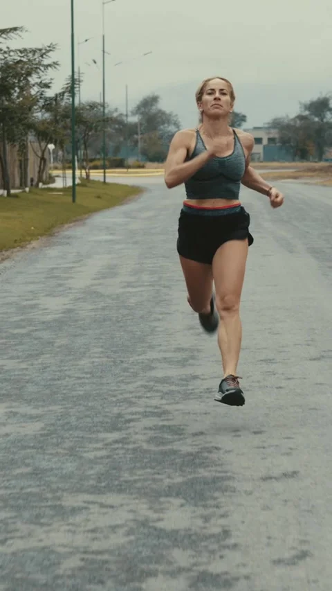 Front tracking shot of female runner passing a tree lined road Stock Footage 340046945
