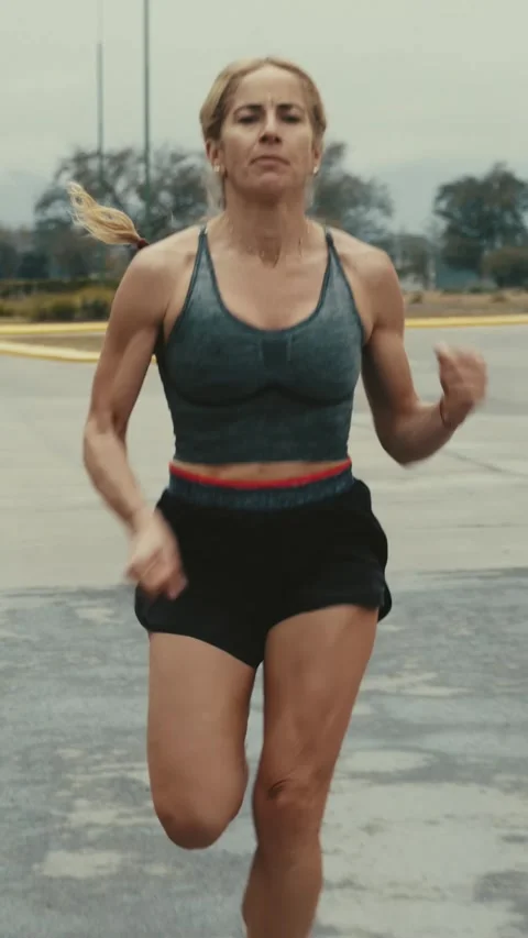 Front tracking shot of female runner sprinting along a road Stock Footage 340047010