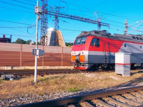 The front of a train racing along the rails against the backdrop of a fence and Stock Photos