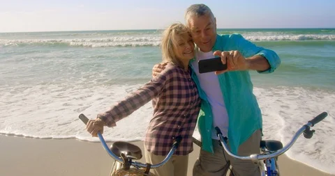Front view of active senior Caucasian couple taking selfie with mobile phone on Stock Footage 106904690