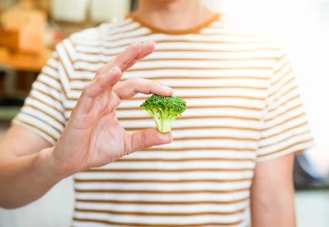 Front view and selective focus of man in striped t shirt holding broccoli piece Stockfoto's