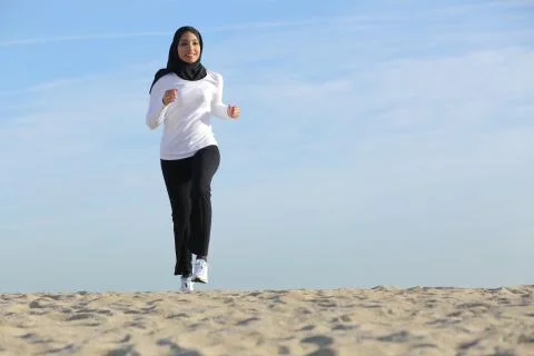 Front view of an arab saudi emirates woman running on the beach Stock Photos