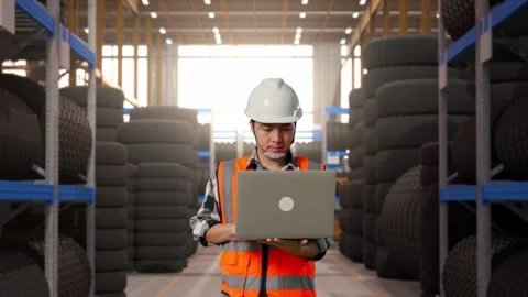 Front View of Asian Male Engineer Use Computer While Walking at Tire Warehouse Stock Footage 341784276