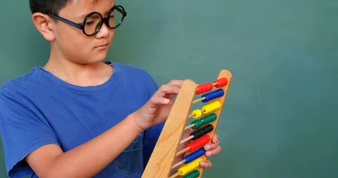 Front view of Asian schoolboy solving math problem with abacus in a classroom at Stock Footage 106931125