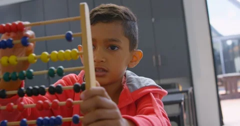 Front view of Asian schoolboy solving math problem with abacus at desk in a Stock Footage 106934733
