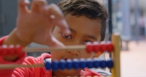 Front view of Asian schoolboy solving math problem with abacus at desk in a Stock Footage 106934779