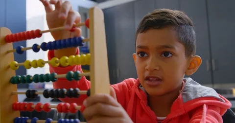 Front view of Asian schoolboy solving math problem with abacus at desk in a Stock Footage 106934877