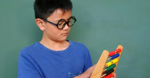 Front view of Asian schoolboy solving math problem with abacus in a classroom at Stock Photos