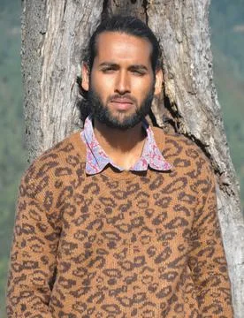 Front view of a bearded young guy looking at camera while leaning against tree   Stock Photos