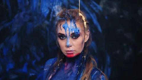 Front view of a beautiful lady in blue paint, pouring the yellow paint from the Stock Footage 89579946