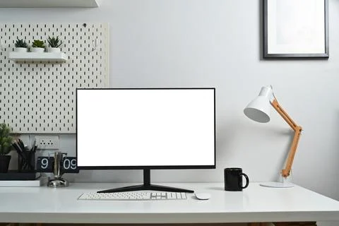 Front view of blank computer desktop, lamp, clock and supplies on white table Stock Photos