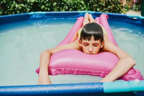 Front view of a blonde boy lying on a pink float resting in a pool. 写真素材