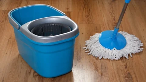 Front view of a blue bucket and a flat wet mop wiping slowly the parquet in the Stock Footage 122380456