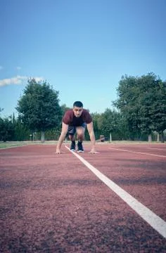 Front view with blue sky background of an athlete starting his career on a track Stock Photos