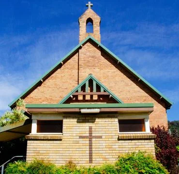 Front View Of A Brick Church With Green Roof And Cross Against A Clear Blue S Stock Photos