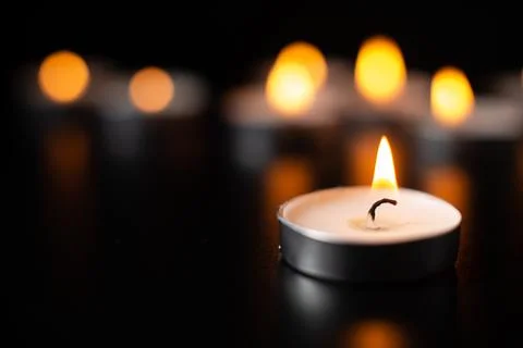 Front view of burning candles on pitch black surface funeral war evil death.. Stock Photos