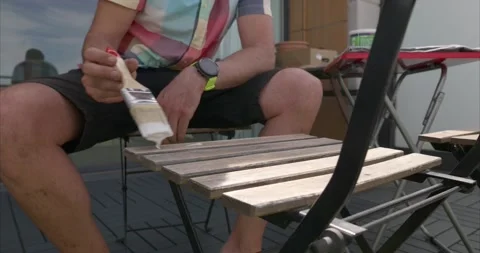 Front view close-up of a man varnishing a chair on the terrace of his house o Stock Footage 155276768
