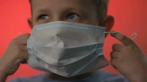 A front view closeup of a young blonde boy trying to put on a virus mask but not Stock Footage 129571999