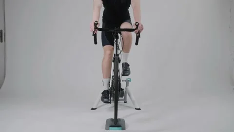 Front view of a cyclist training on an exercise bike in bright white studio Video stock 171117379