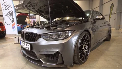 Front view of a dark gray BMW M4 with the lifted hood at a car exhibition, Stock Footage 158008358