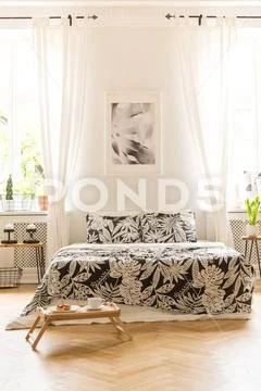 Front view of a double bed with floral sheets, graphic on the wall between wi Stock Photos