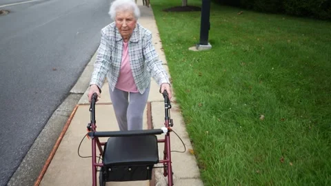 Front view of elderly senior old woman using walker for mobility on sidewalk for Stock Footage 252597236