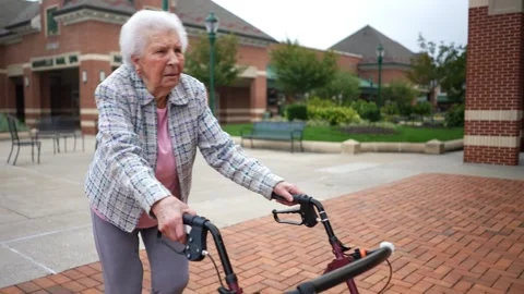 Front view of elderly senior old woman using walker for mobility on sidewalk at Stock Footage 253404556