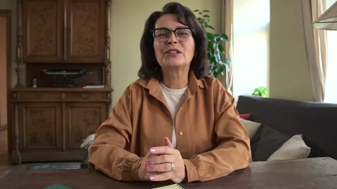 Front view of elderly woman talking and waving at table in home room. Video stock 149388031