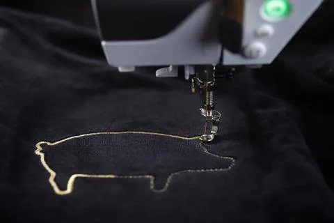 Front view on embroidery machine stitching pig motive with gold yarn Stock Photos