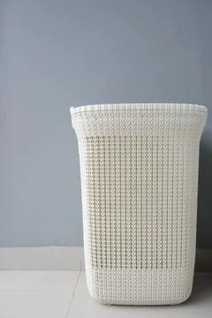 Front view of an empty white woven plastic laundry basket on a tiled floor Stock Photos