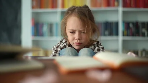 Front view of exhausted upset primary child school girl sitting alone hugging Video stock 159762143