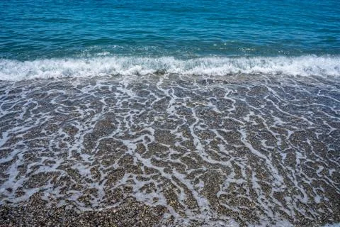 Front view of foamy wave reaching the calm beach with pebbles Stock Photos