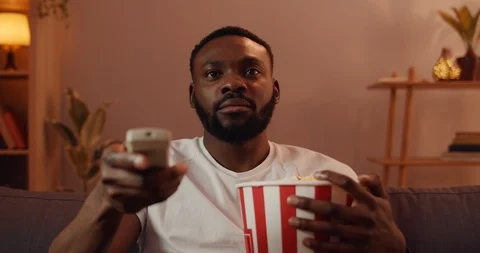 Front view of good looking guy switching on TV and watching television program Video stock 127157173