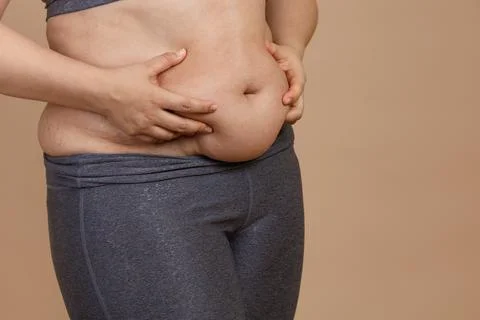 Front view of hands squeezing extra weight big belly of lady in leggings. Body Stock Photos