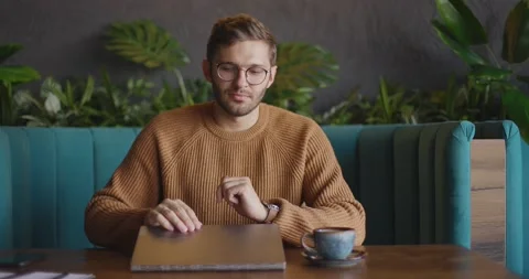 Front view of handsome man in eyeglasses in brown sweater finishes work at Stock Footage 164715327
