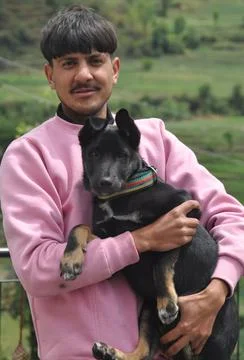 Front view of a handsome young guy standing outdoor with holding black color dog Stock Photos