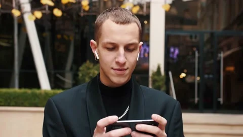Front view of a happy man walking towards camera using a smartphone, playing or Stock Footage 143877389